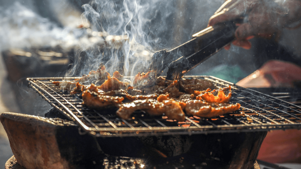 a person grilling meat on a grill with smoke coming out of it