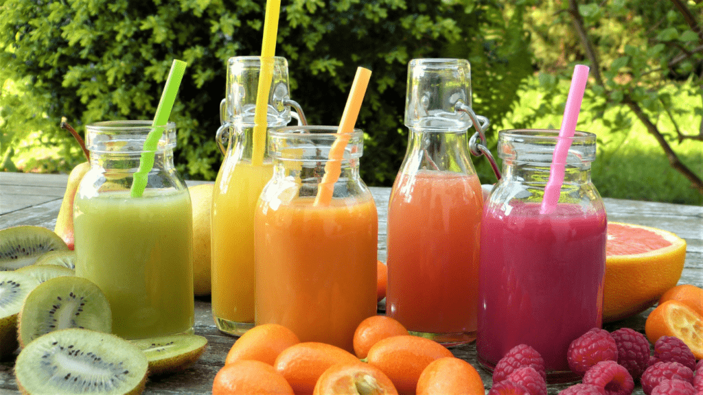 various fruits and juices are sitting on a wooden table